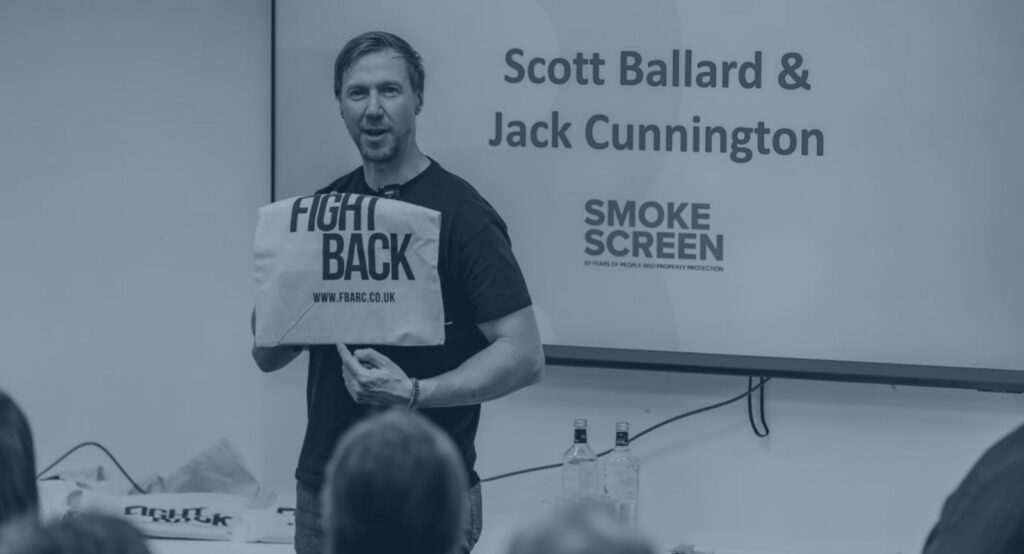 Scott Ballard presenting at a Fight Back Against Retail Crime event with FBARC tote bag and Smoke Screen branding on screen