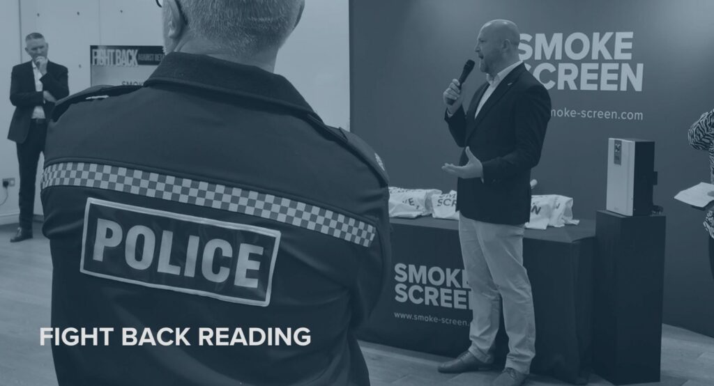 Matt Gilmartin presenting at Fight Back Reading event, Smoke Screen branding on display, police officer and audience in attendance